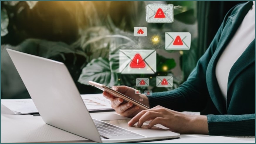 Woman typing on laptop keyboard with email warning symbols floating above.