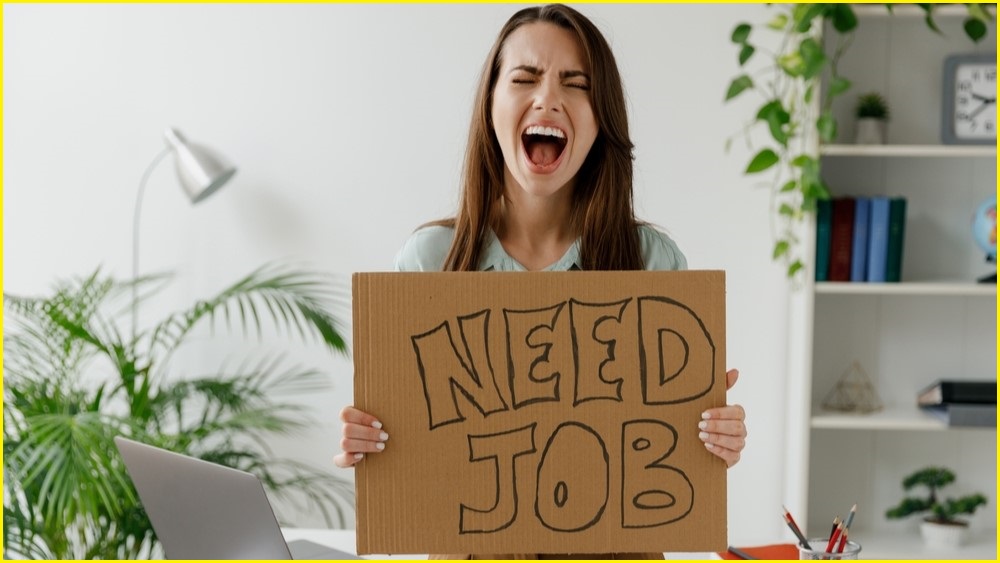 Frustrated woman holding placard that reads 'NEED JOB'.