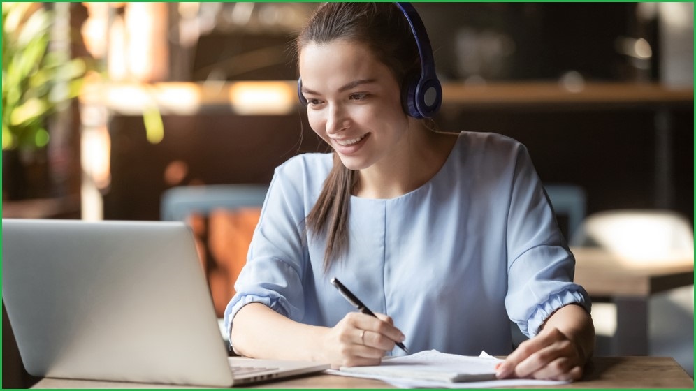 Woman working from home at laptop, wearing headphones.