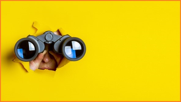 A pair of binoculars poking out of a yellow background