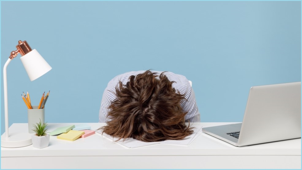 Woman sitting at a desk with her head down on the table.