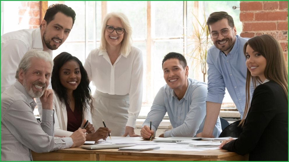 A diverse group of office employees standing around a table.