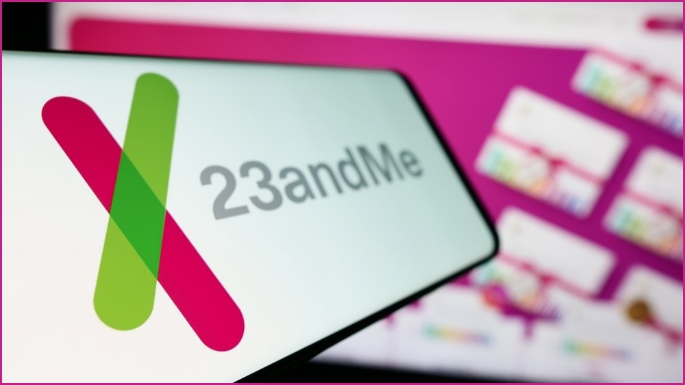 23andMe logo on a phone screen being held up in front of a computer screen.