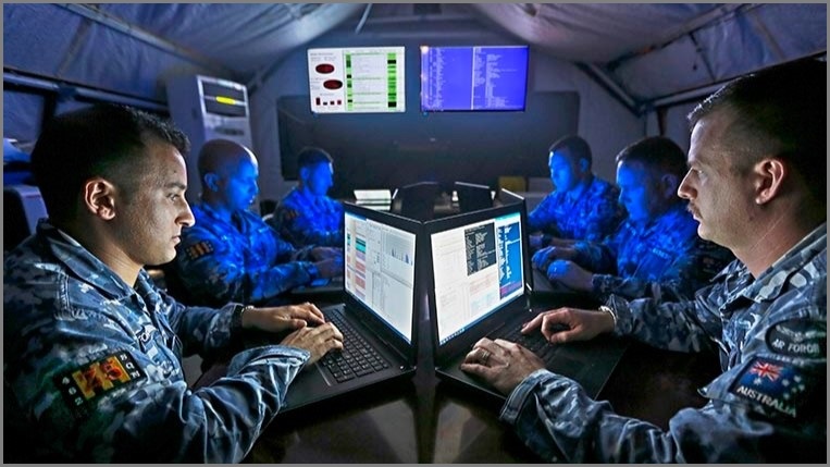 Men in uniform sitting around computers in a tent.