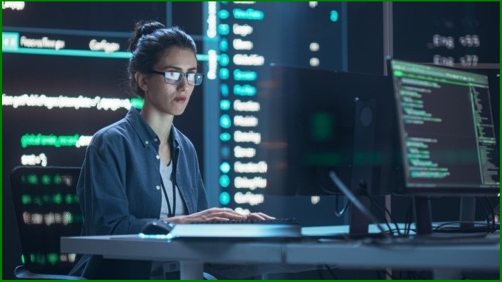 Woman sitting at a computer, surrounded by monitors.