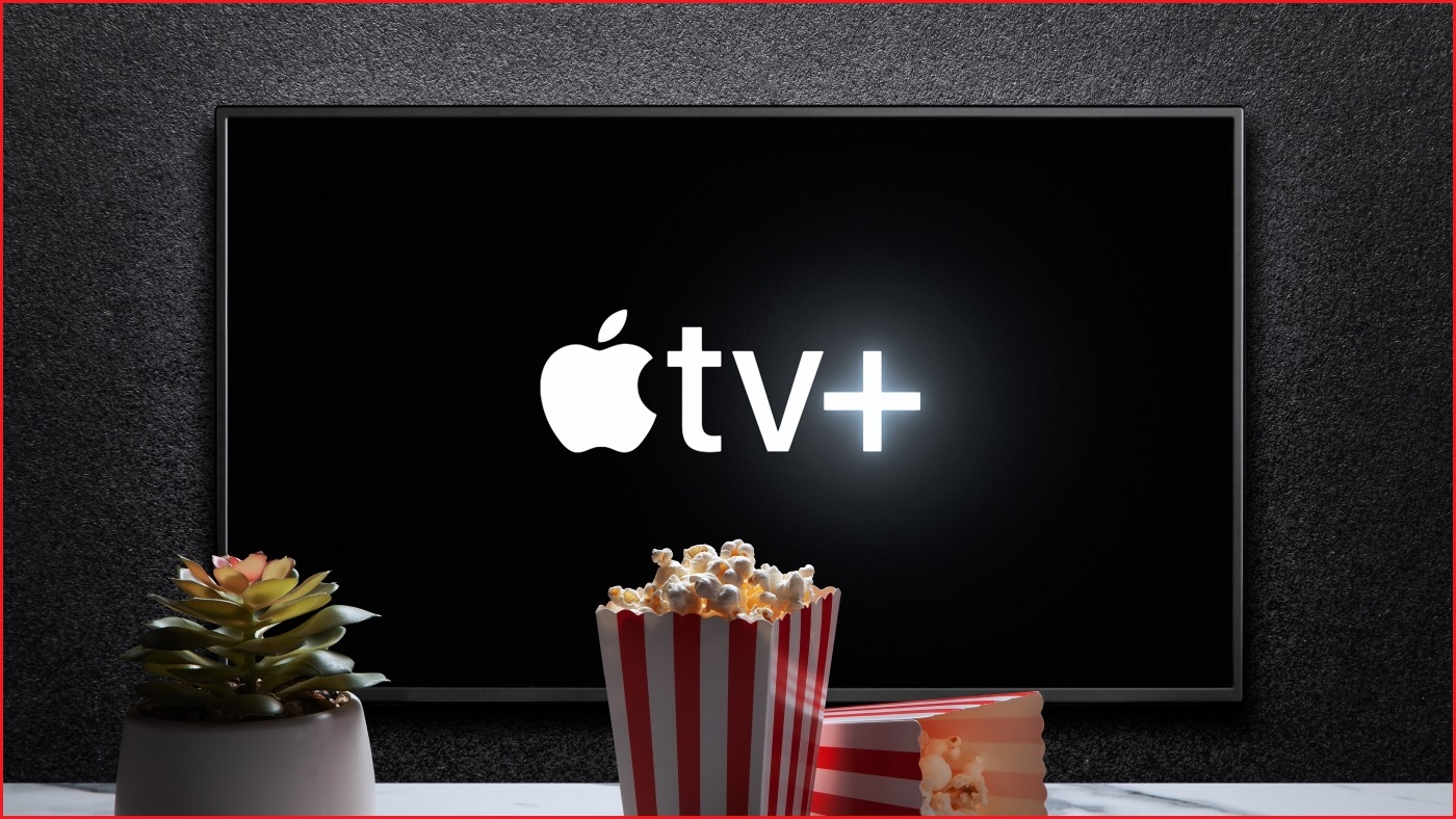 A medium shot of a TV displaying the Apple TV+ logo, with popcorn and a small plant on a table in the foreground.