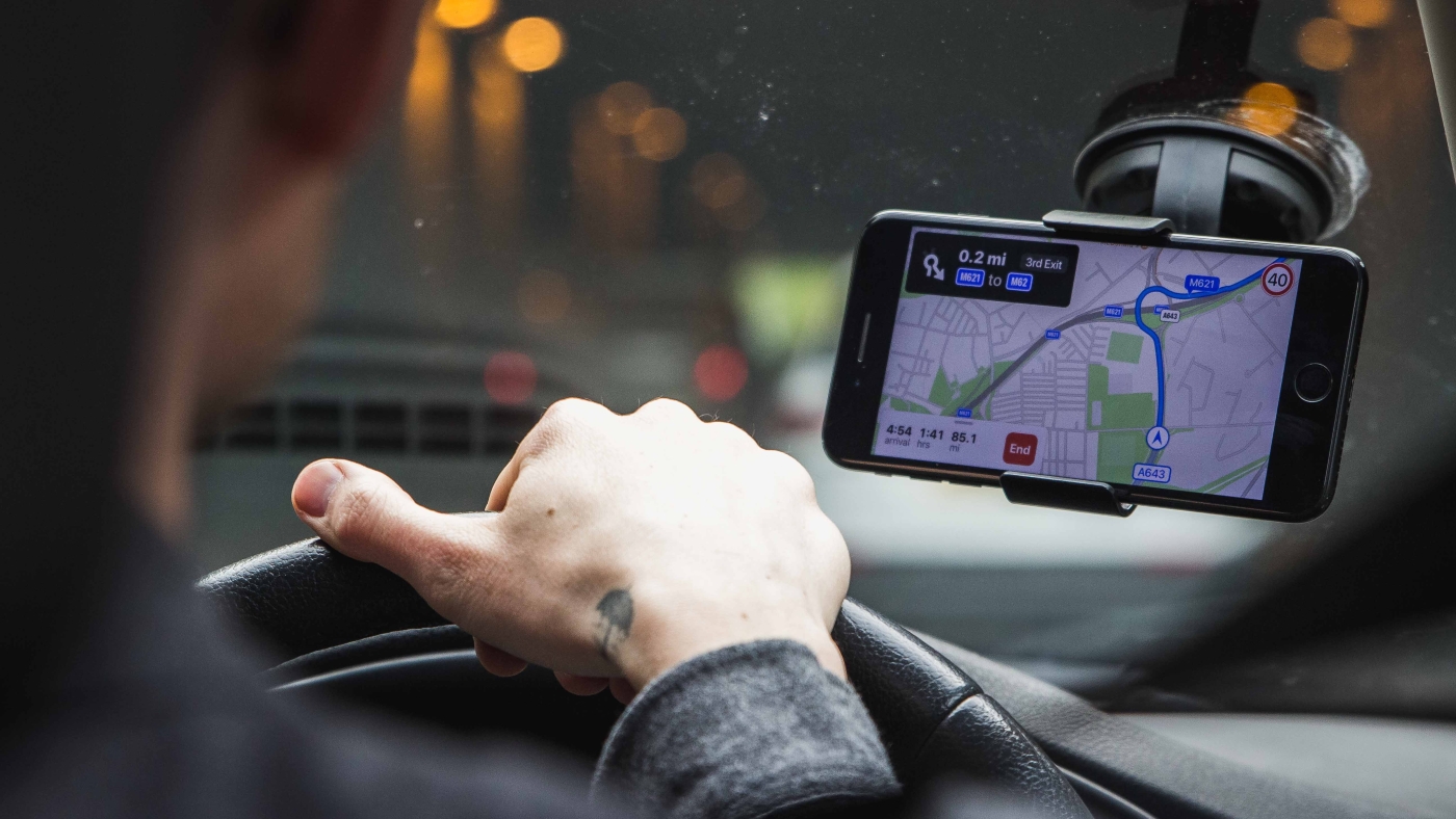 An over-the-should photo of a person driving a car in a tunnel, with a phone mounted to their windscreen displaying a GPS map