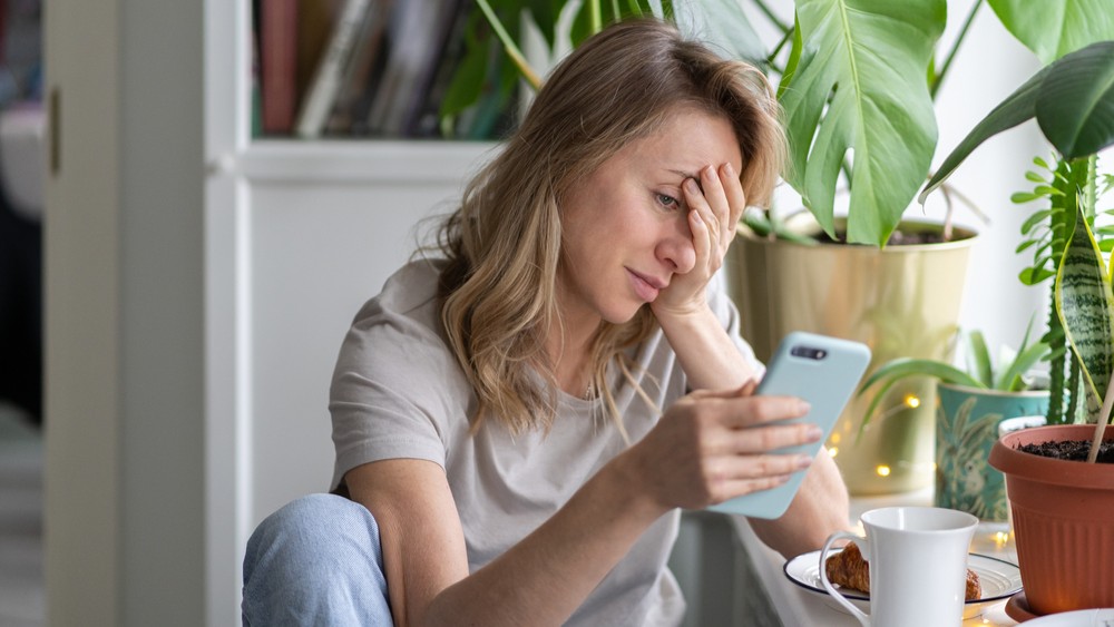 Woman looking at her phone, facepalming herself.