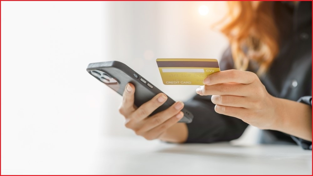 A close up of a person's hands holding a smartphone in one, and a credit card in the other.