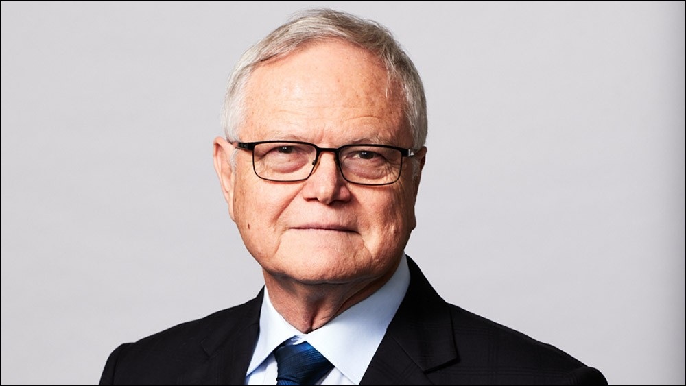 A medium shot of Dr Ben Greene in a suit, tie, and glasses.