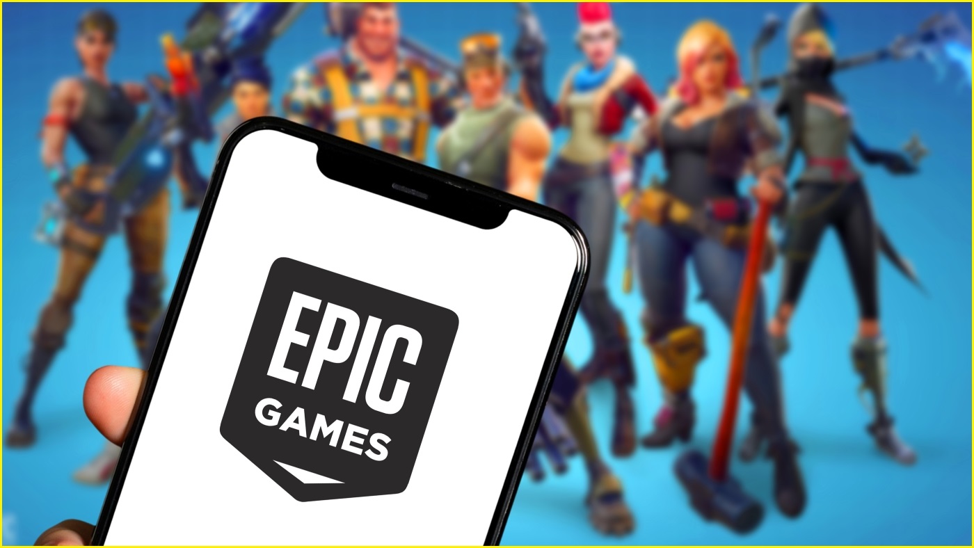 A close up of an iPhone displaying the Epic Games logo. In the background, a blurred image of characters from Fortnite.