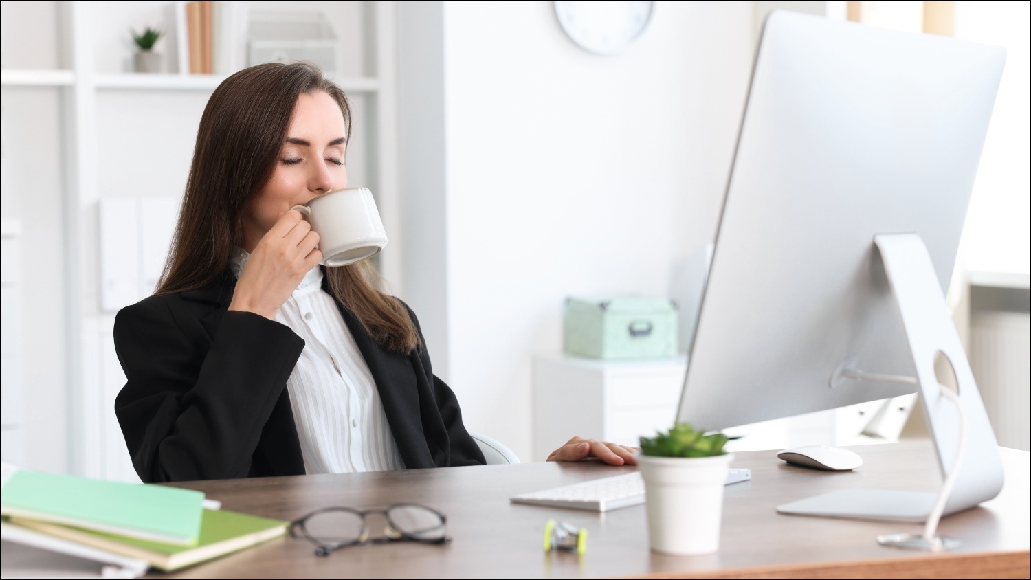 A female worker sitting in front of a computer at home and happily drinking from a mug.
