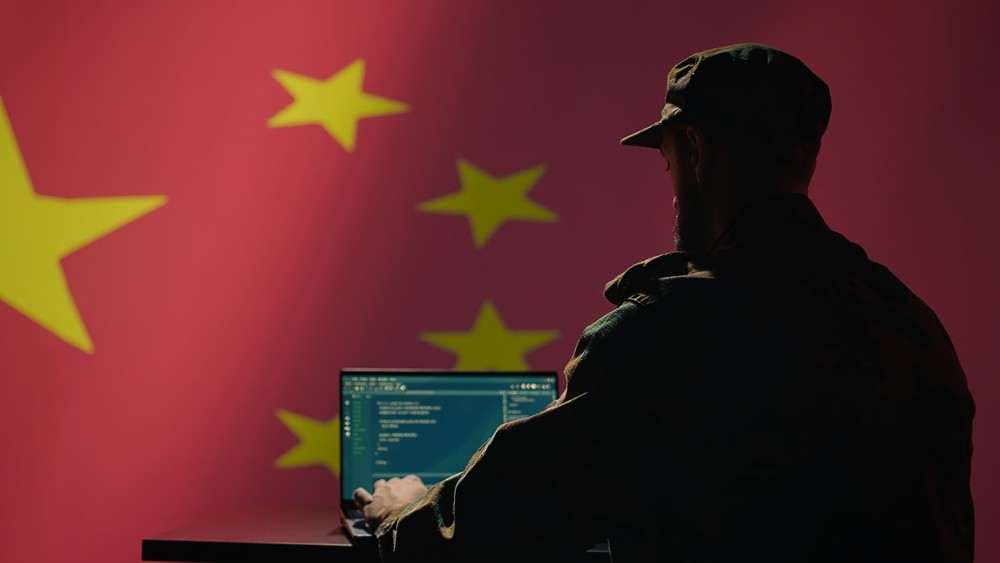 Man sitting at computer with China flag in background.