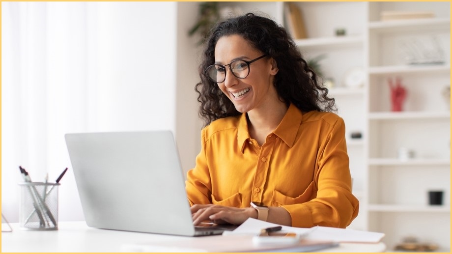 Smiling woman in yellow/orange short typing on a laptop keyboard.