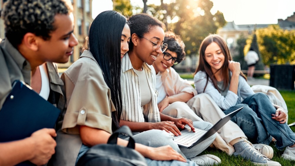 A group of international students doing work on a laptop outdoors.