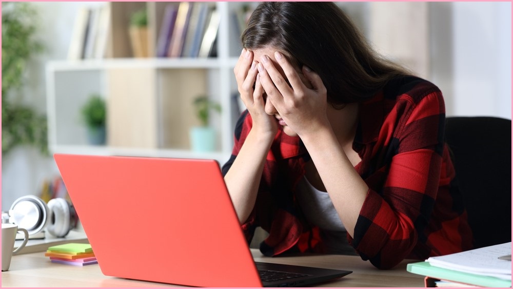 Upset woman covering her eyes while sitting at her laptop.