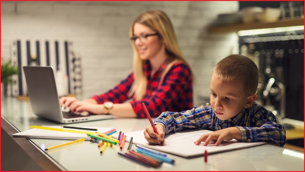 Woman working on a laptop in the background while child draws in the foreground.