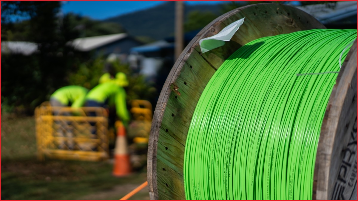 A close up of a wheel of optical fibre cable, with men workin in high-viz shirts in the background.