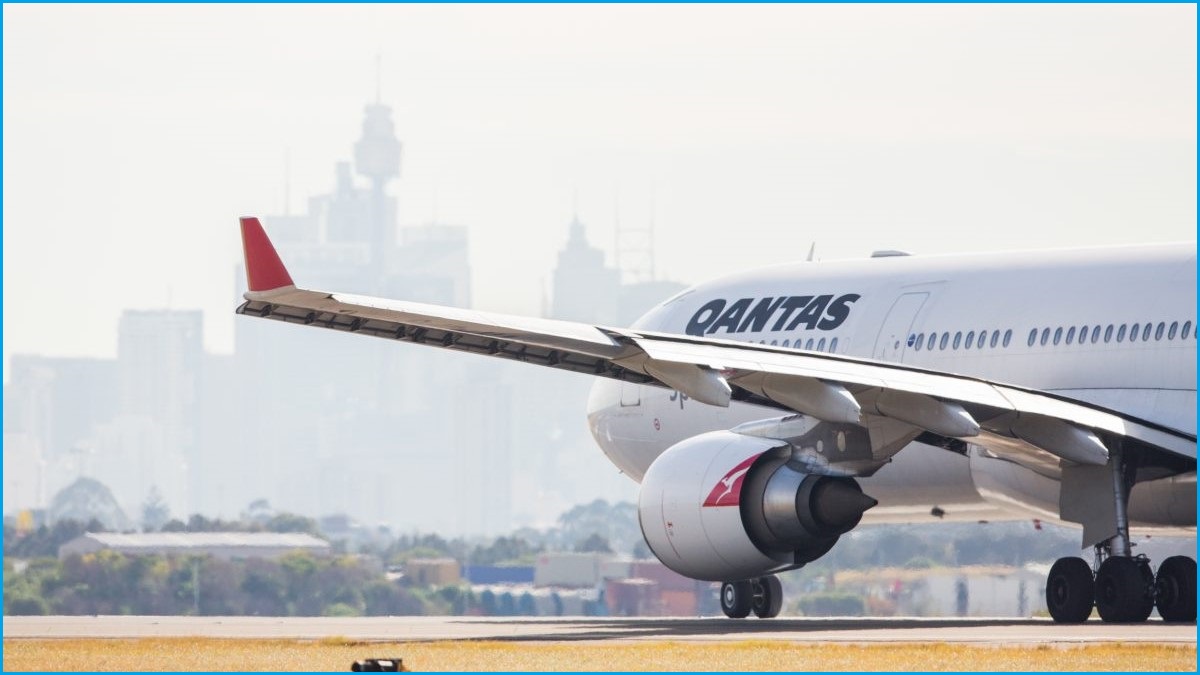 A close up of the side of a Qantas plane on the tarmac, with the Sydney skyline in the background.