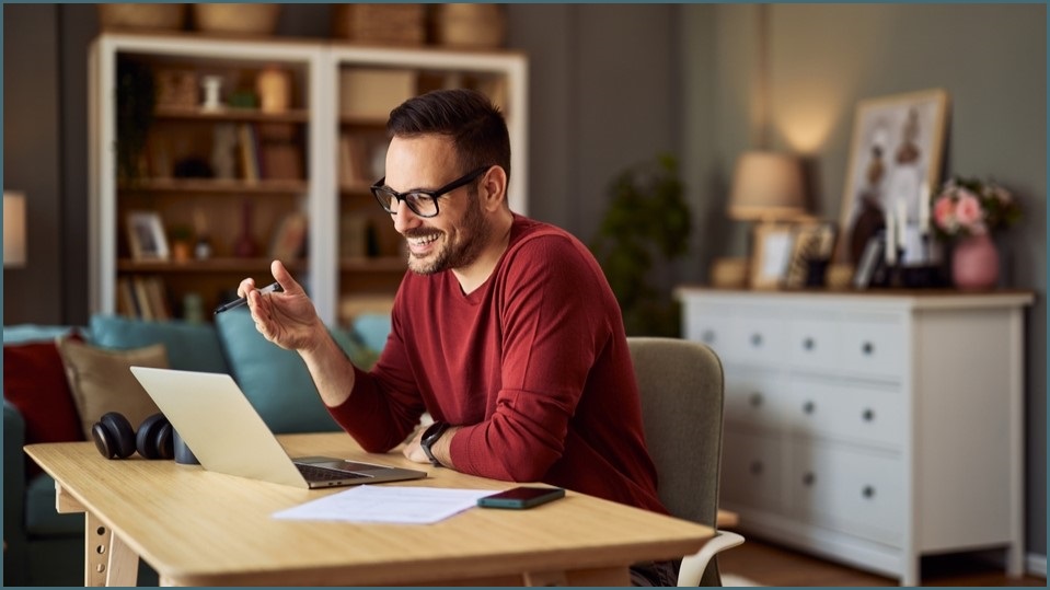 Man smiling, looking at a laptop screen, working from home.
