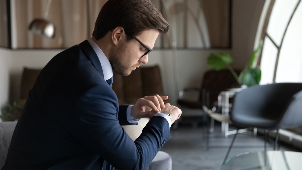 Seated man in suit looking at his watch.