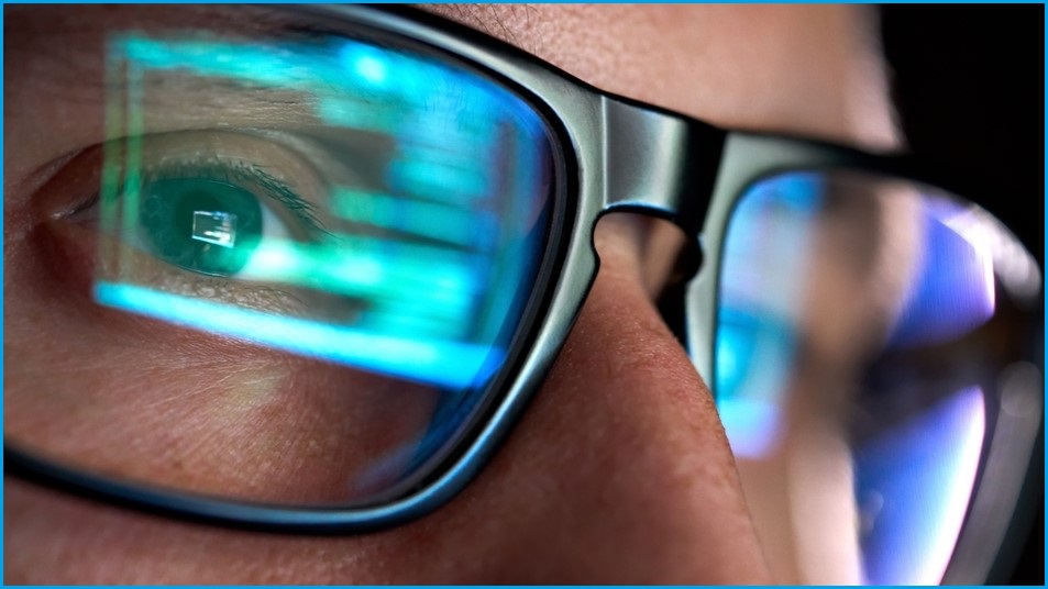 A close up of the eyes of someone who is wearing glasses, on which a computer screen is reflected.