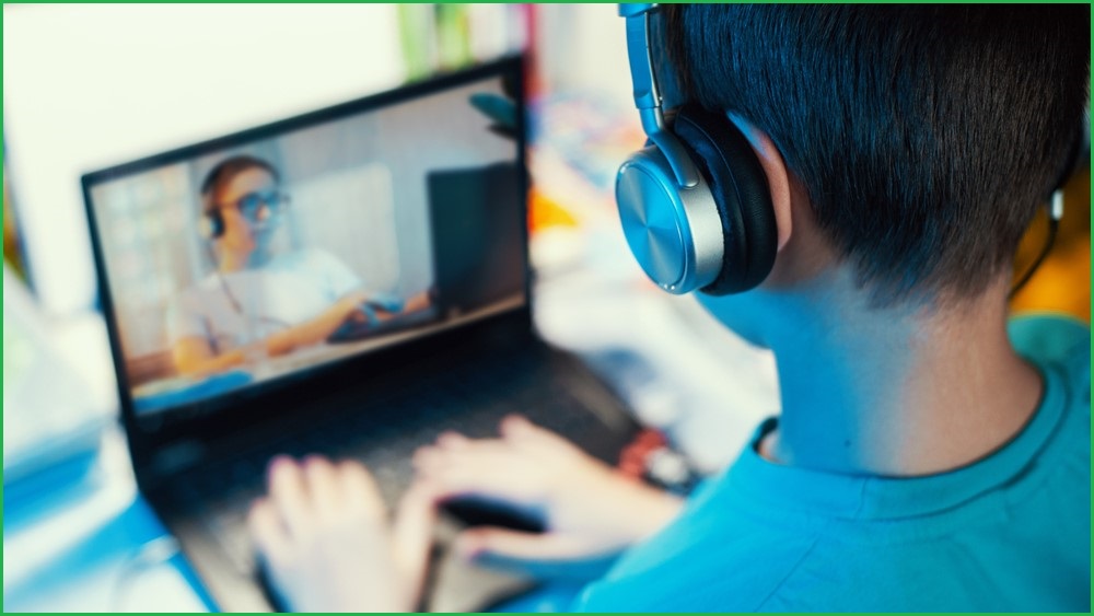 An over-the-shoulder photo of a teenage boy using a laptop, which is displaying an image of a young woman also using a laptop.