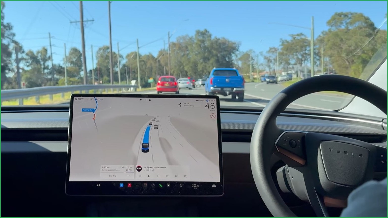 A medium shot of the steering wheel and main screen inside the interior of a tesla, driving on an Australian road.
