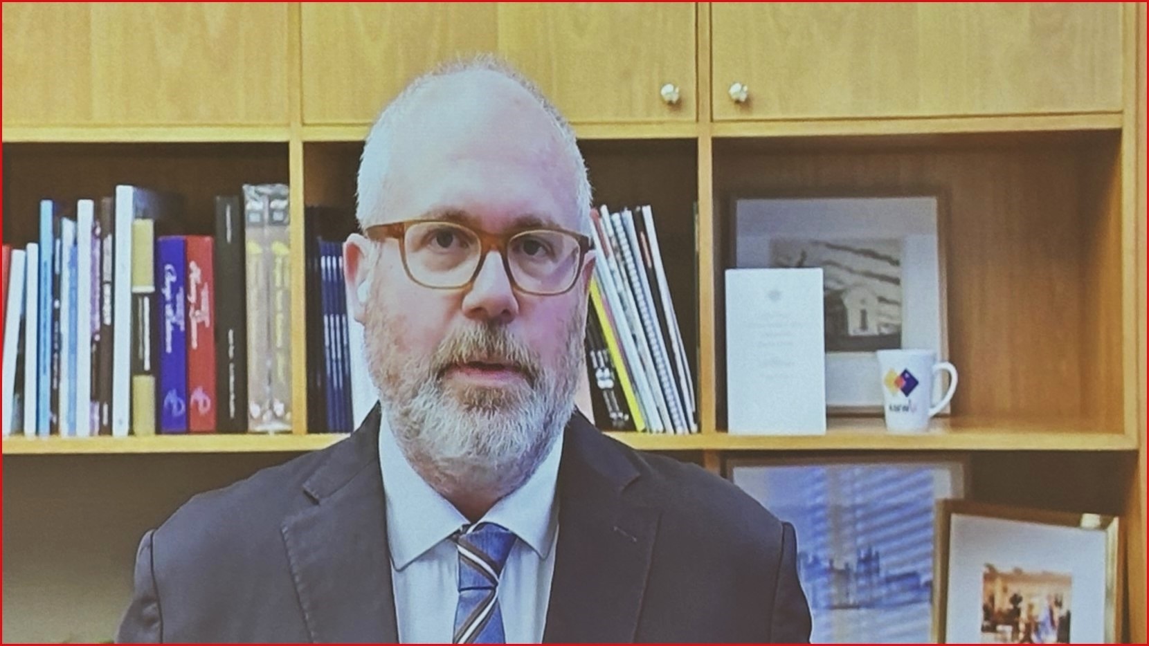 A close up Tim Ayres in a suit and tie, speaking in front of a bookcase.