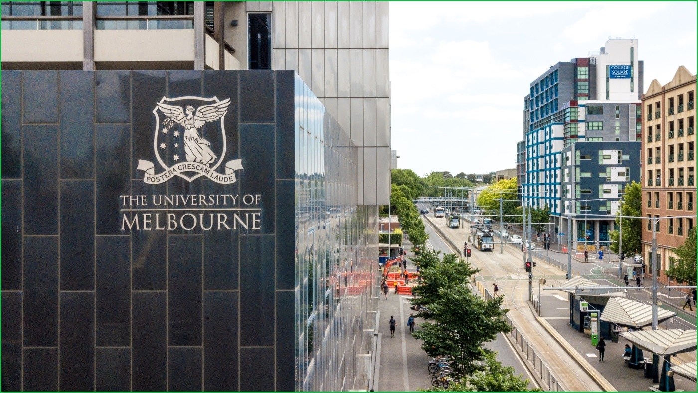 A wide outdoor shot of a University of Melbourne building with a logo on its side, next to a Melbourne street with tram tracks.