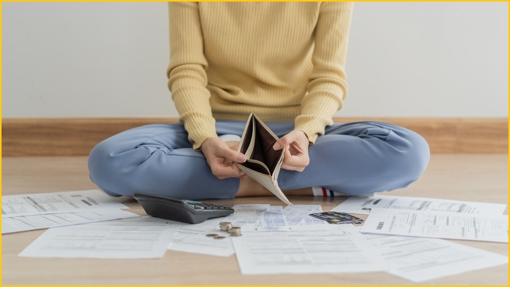 Person sitting on floor holding open an empty wallet.