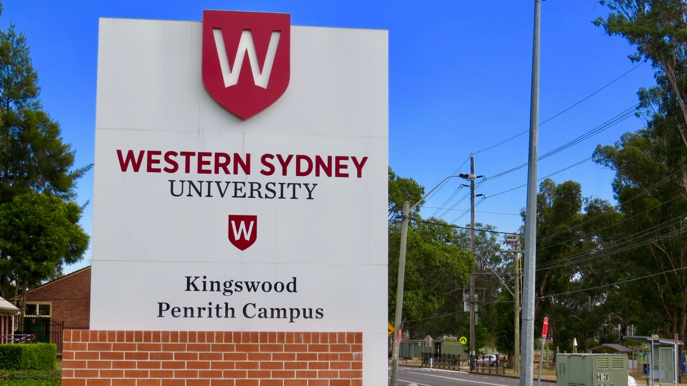 A medium shot of a sign outside Western Sydney University's Kingswood campus, containing the logo and name of the campus.