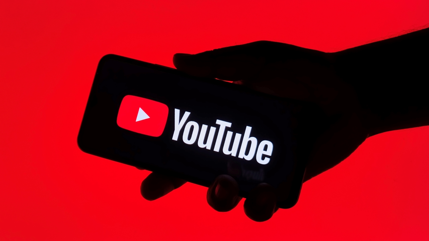 A close up of a person's hand holding a smartphone displaying the YouTube logo.