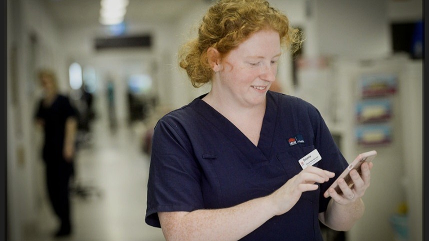 Nurse in a ward looking at a device screen.
