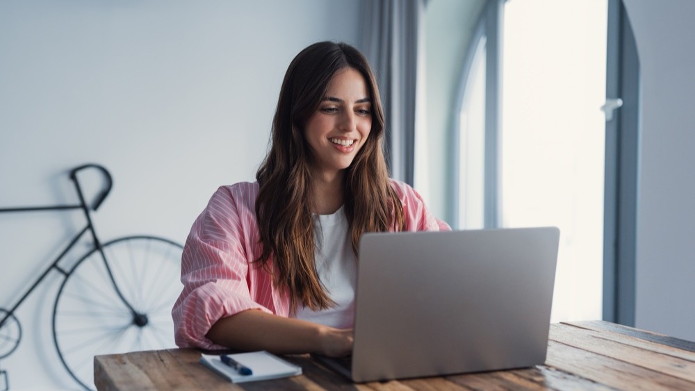 Smiling young woman in pink shirt using a laptop.