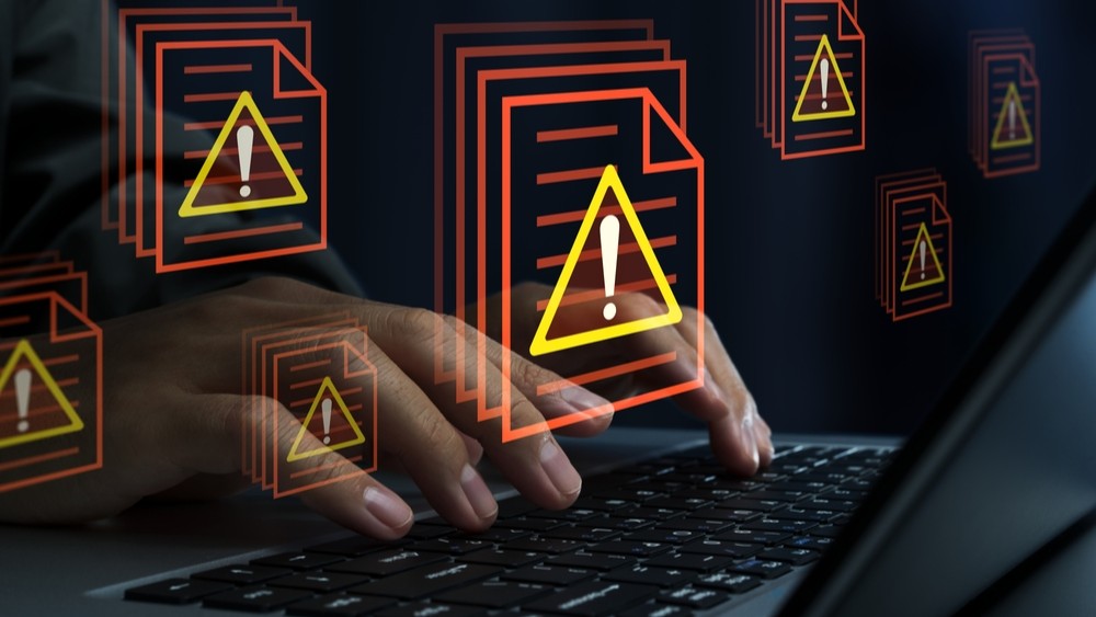 Fingers typing on laptop keyboard with warning symbols floating above.