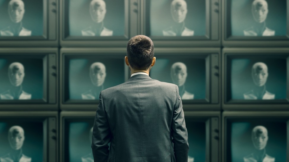 Man looking at wall of TV screens showing robot reading news.