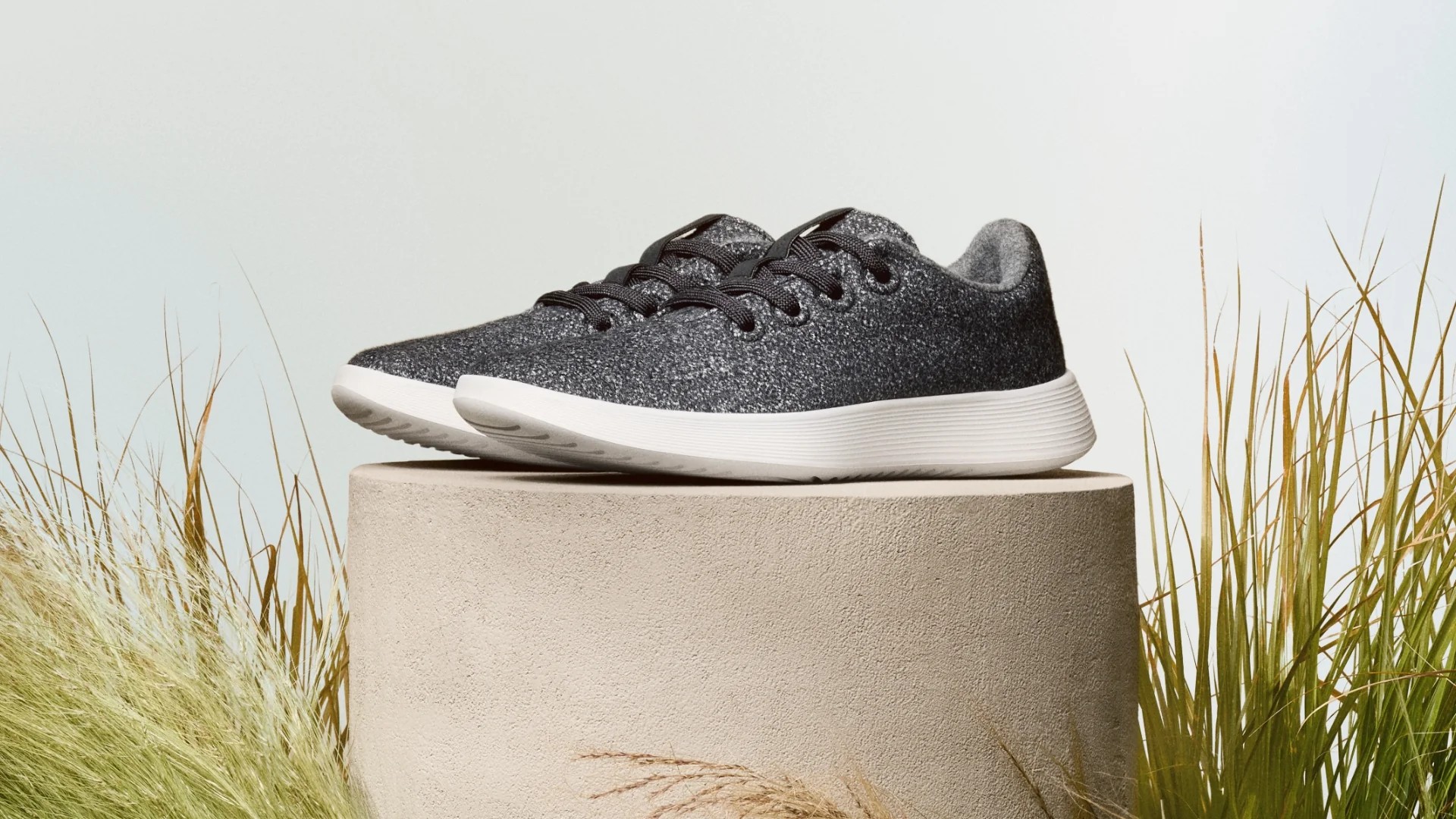 A medium shot of a pair of Allbirds sneakers on a plinth, surrounded by grass.