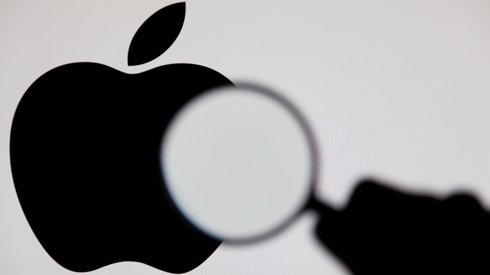A magnifying glass being held over the Apple logo.