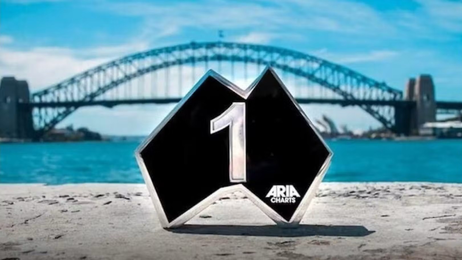 A close up of a #1 ARIA chart award, with the Sydney Harbour Bridge in the backgroun.