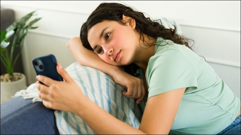 Girl in pale green t-shirt staring wistfully at a phone screen.