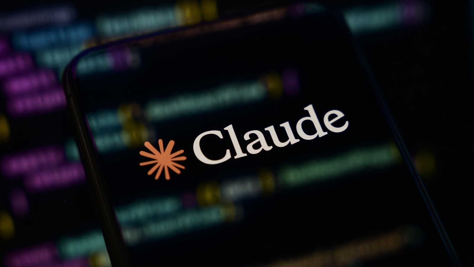 A close up of the Anthropic Claude logo on a smartphone screen, overlaid with computer code.