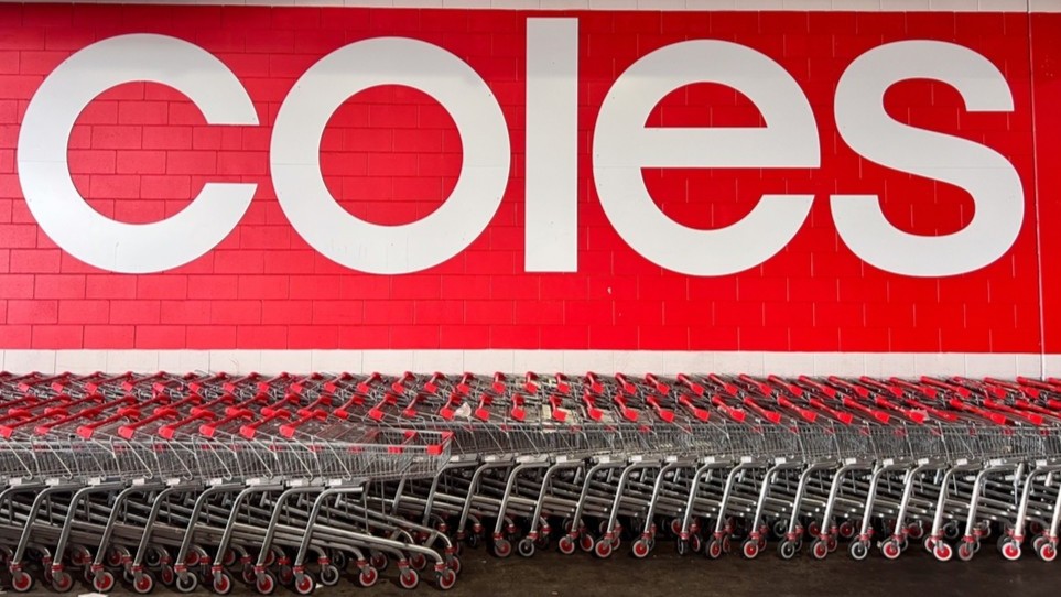 Coles logo on a wall with rows of trolleys in front of it.