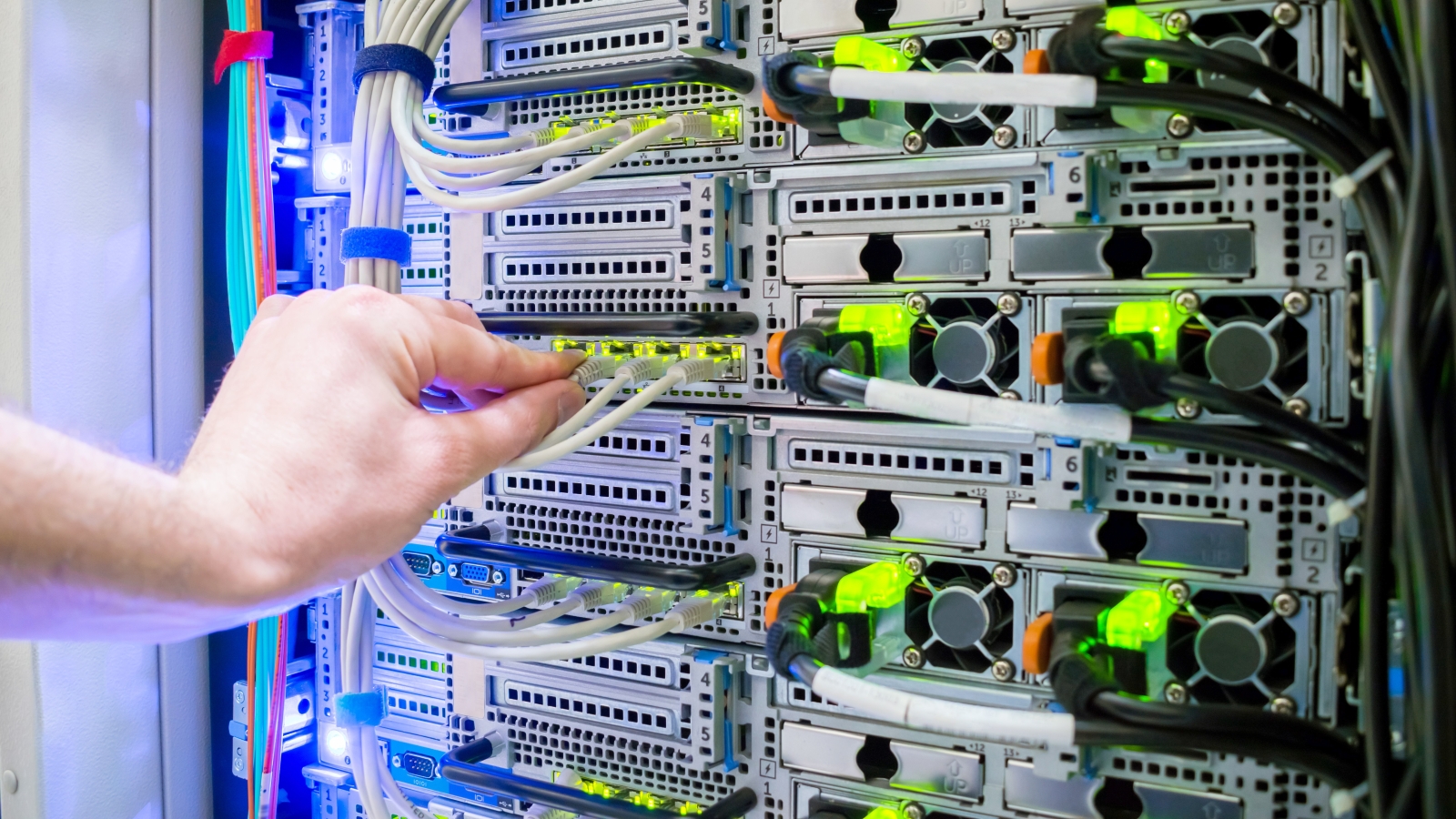 A closeup of a hand holding a cord that's plugged in to a server rack in a data centre.