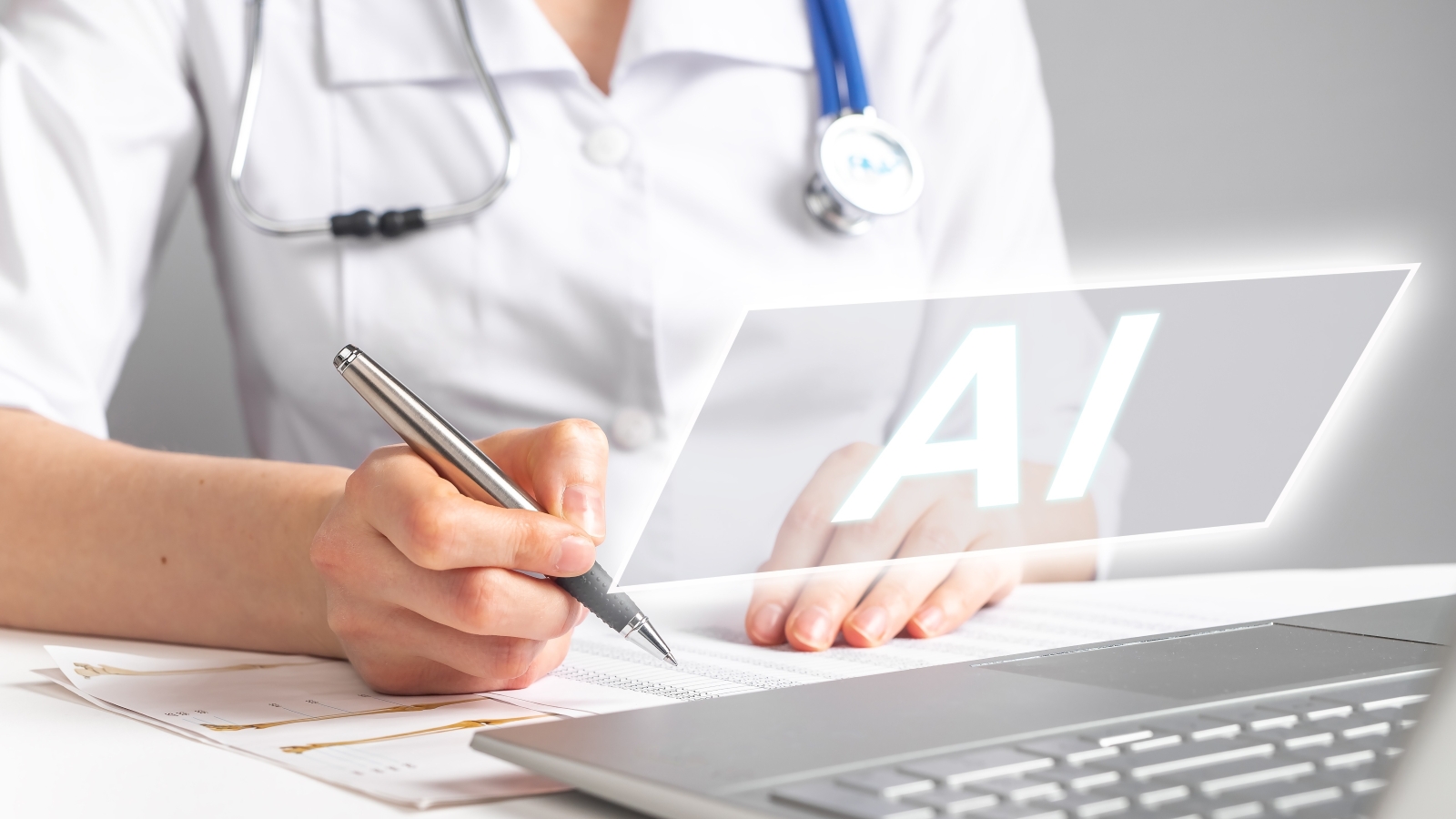 A close up of a doctor's hands, holding a pen and using a laptop. Above the laptop the letters AI float.