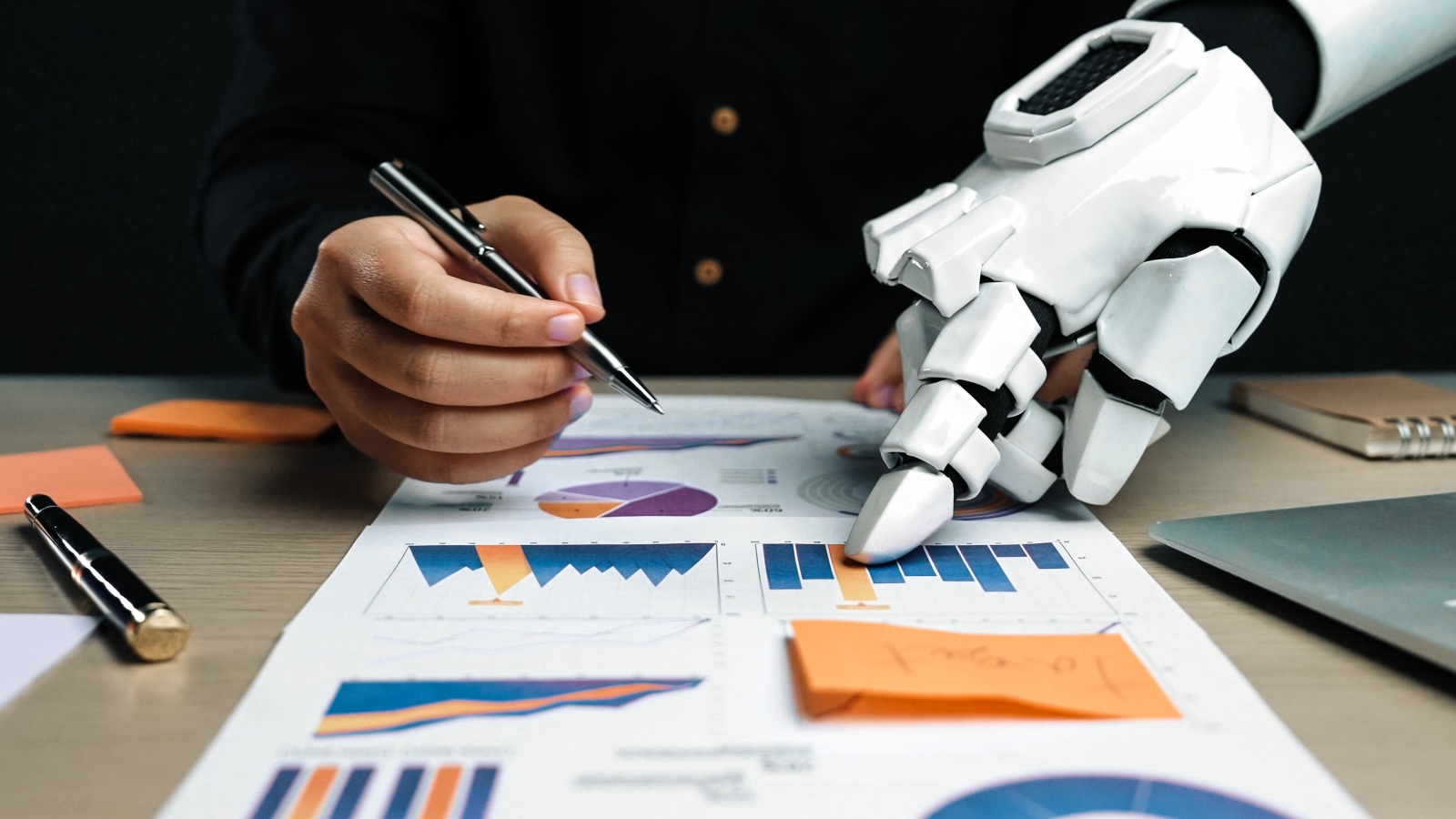A close up of a human hand holding a pen over a printed report, next to a robotic hand pointing at the report.