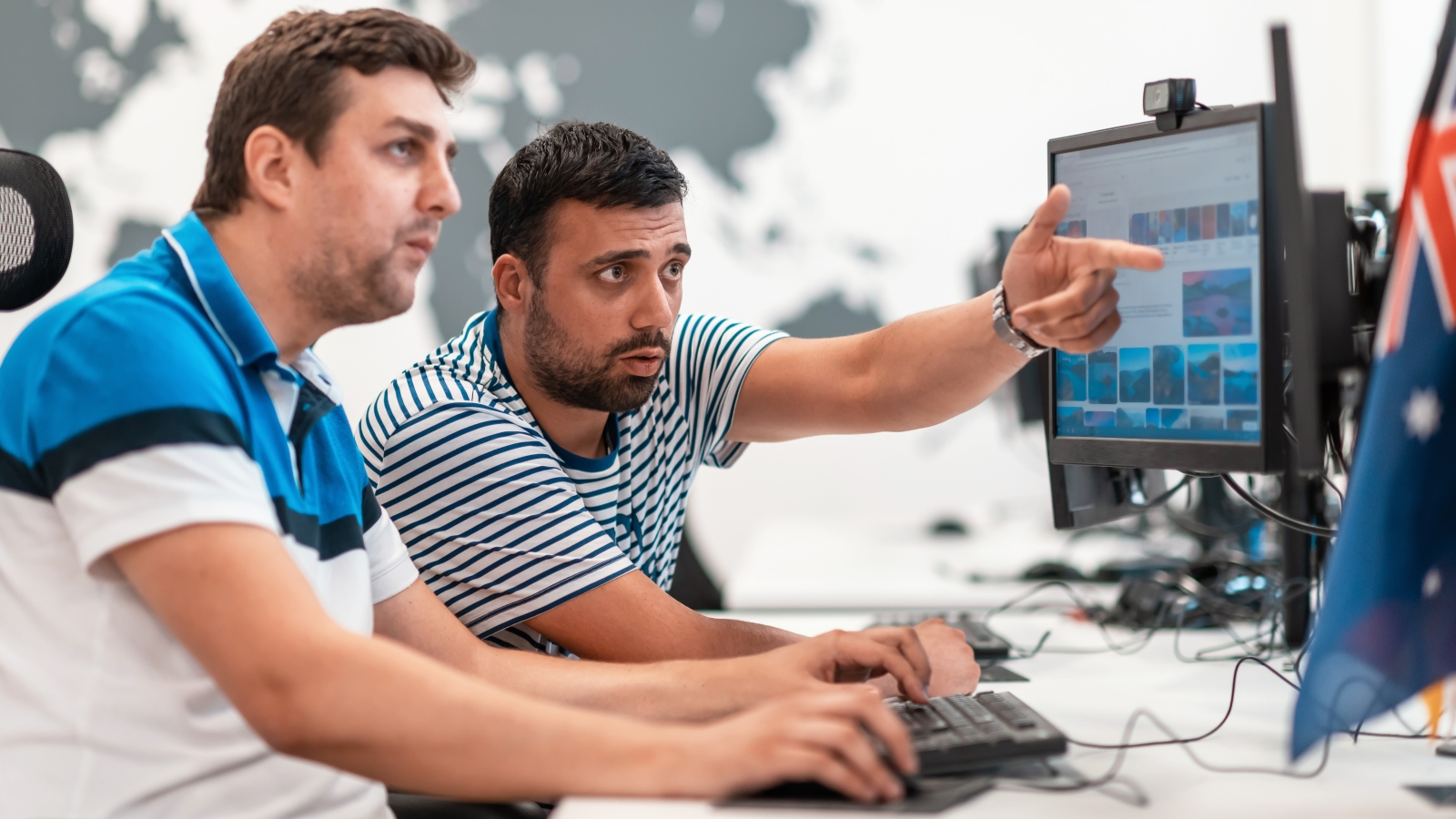 Two men working at computer screens, next to a small Australian flag.