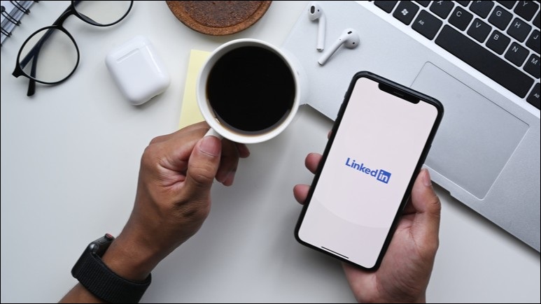 Linkedin logo on phone screen with someone holding cup on coffee in other hand.
