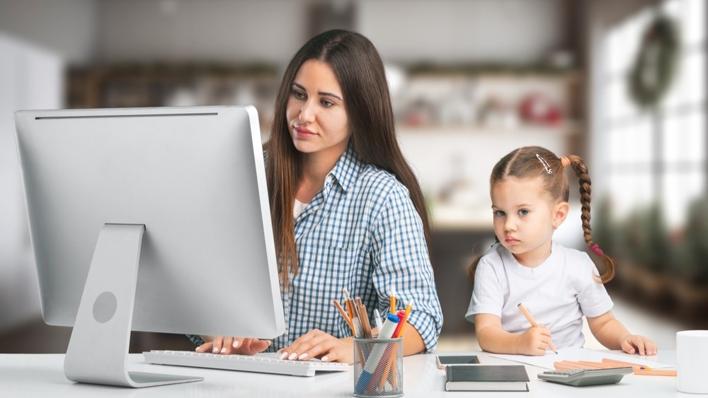 Woman working on a computer with a child seated next to her.