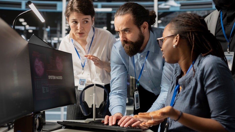 People gathered around a computer screen reading 'SYSTEM HACKED'.
